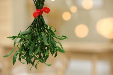 Mistletoe bunch with red bow on blurred background, space for text. Traditional Christmas decor