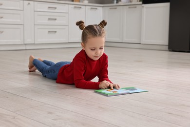 Photo of Cute little girl reading book on warm floor in kitchen, space for text. Heating system