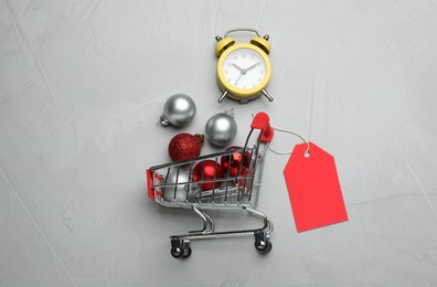 Shopping cart with Christmas decor and alarm clock on grey background, flat lay. Sale concept