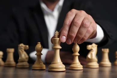Man with chess pieces at wooden table against dark background, closeup