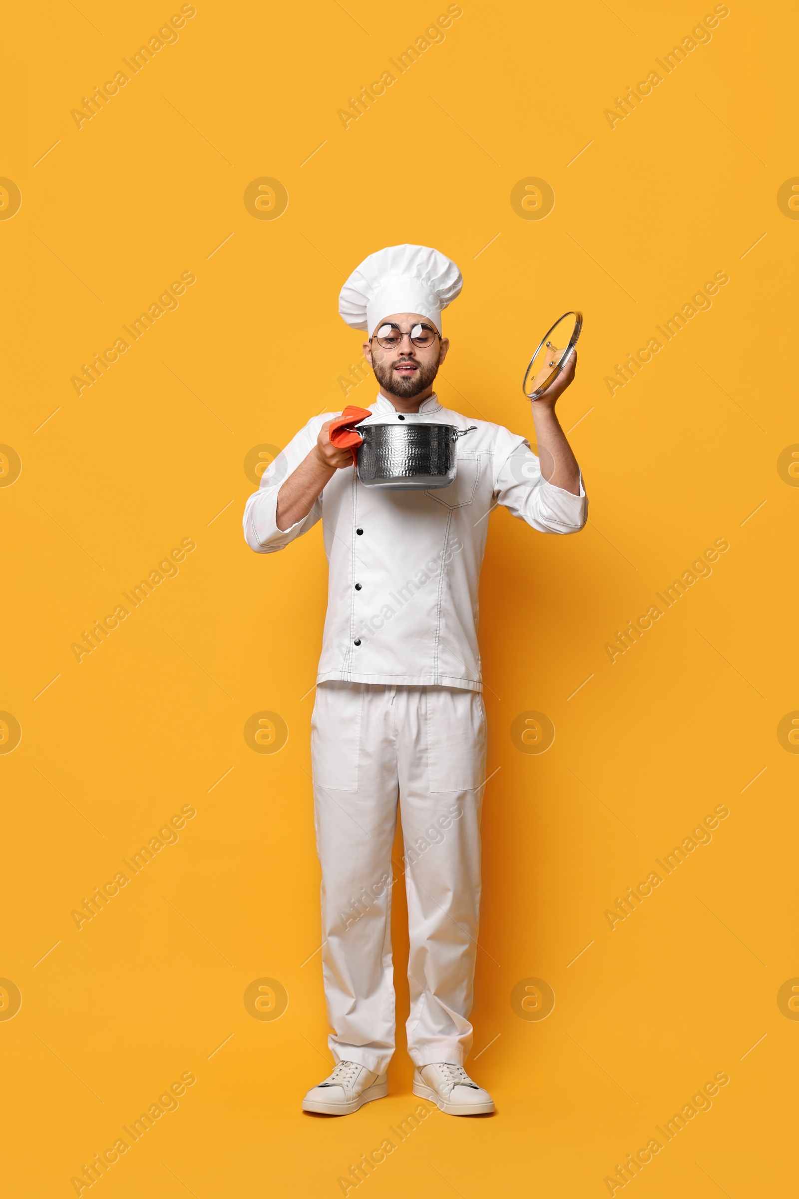 Photo of Professional chef smelling something in cooking pot on yellow background