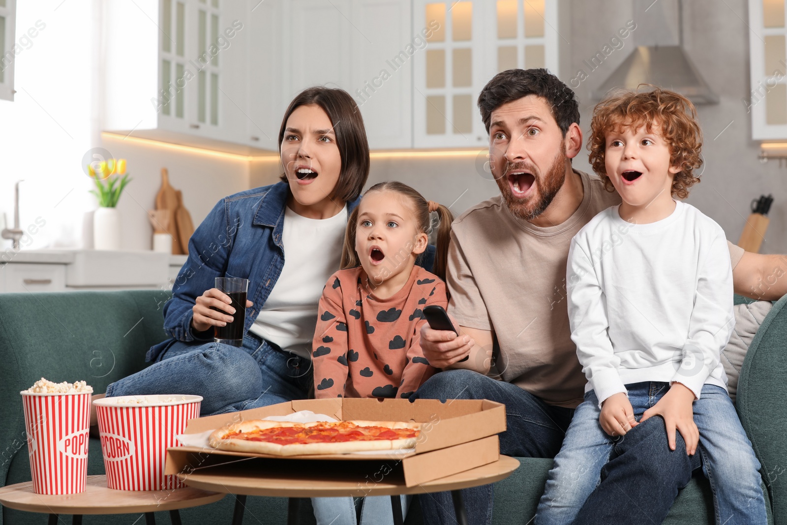 Photo of Surprised family watching TV with popcorn and pizza on sofa at home