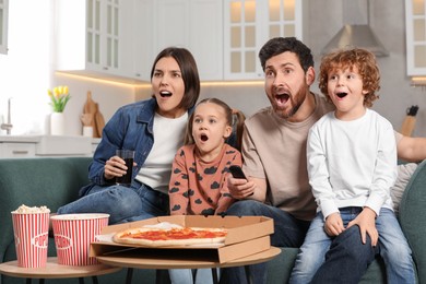 Photo of Surprised family watching TV with popcorn and pizza on sofa at home