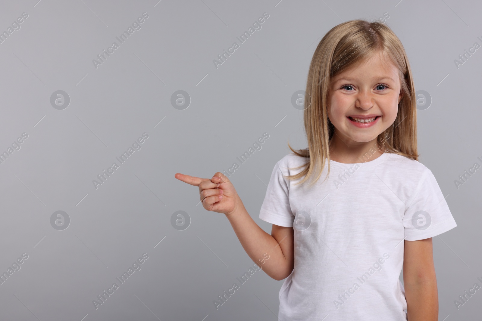 Photo of Special promotion. Smiling girl pointing at something on grey background. Space for text