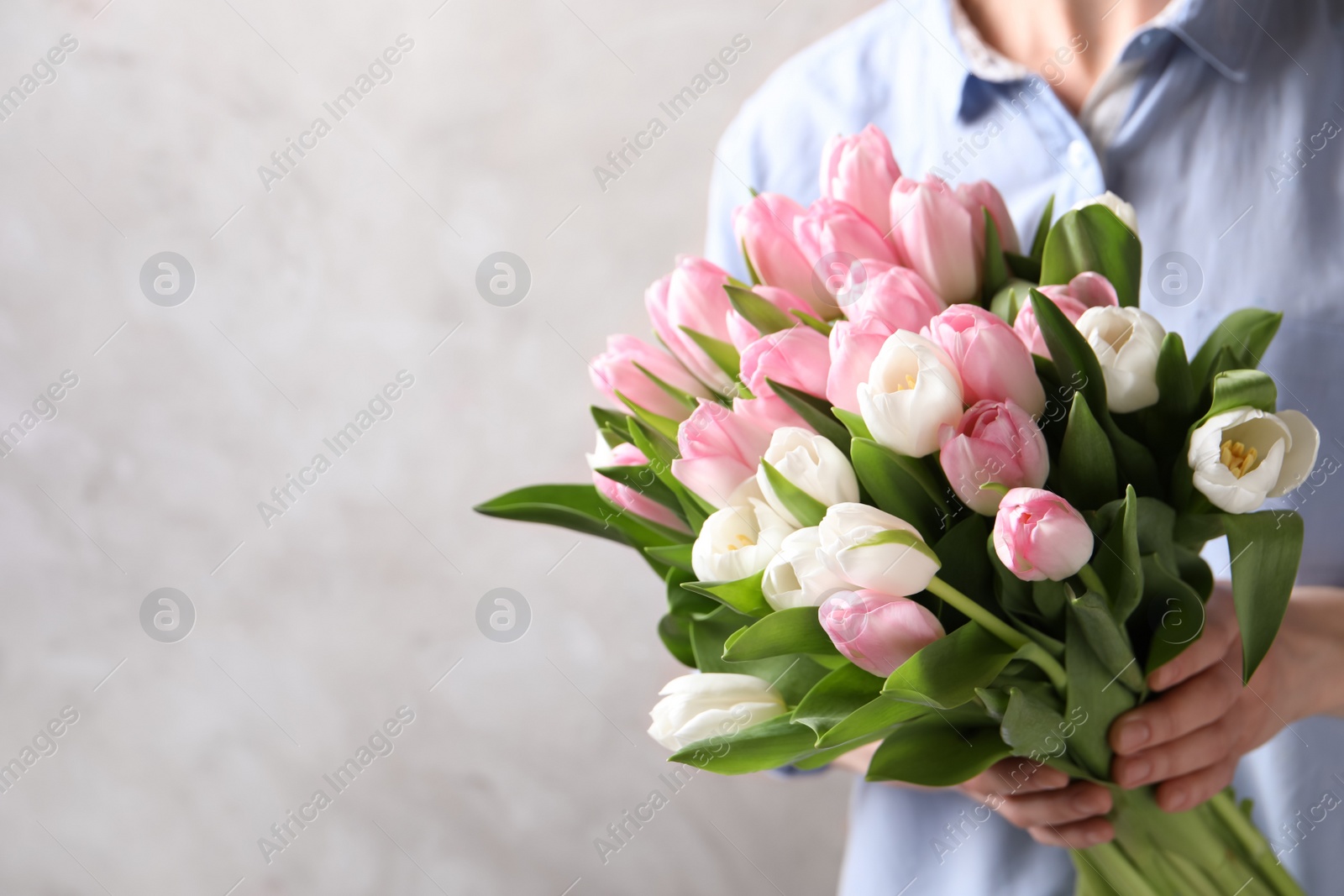 Photo of Woman holding bouquet of tulips against beige background, closeup. Space for text