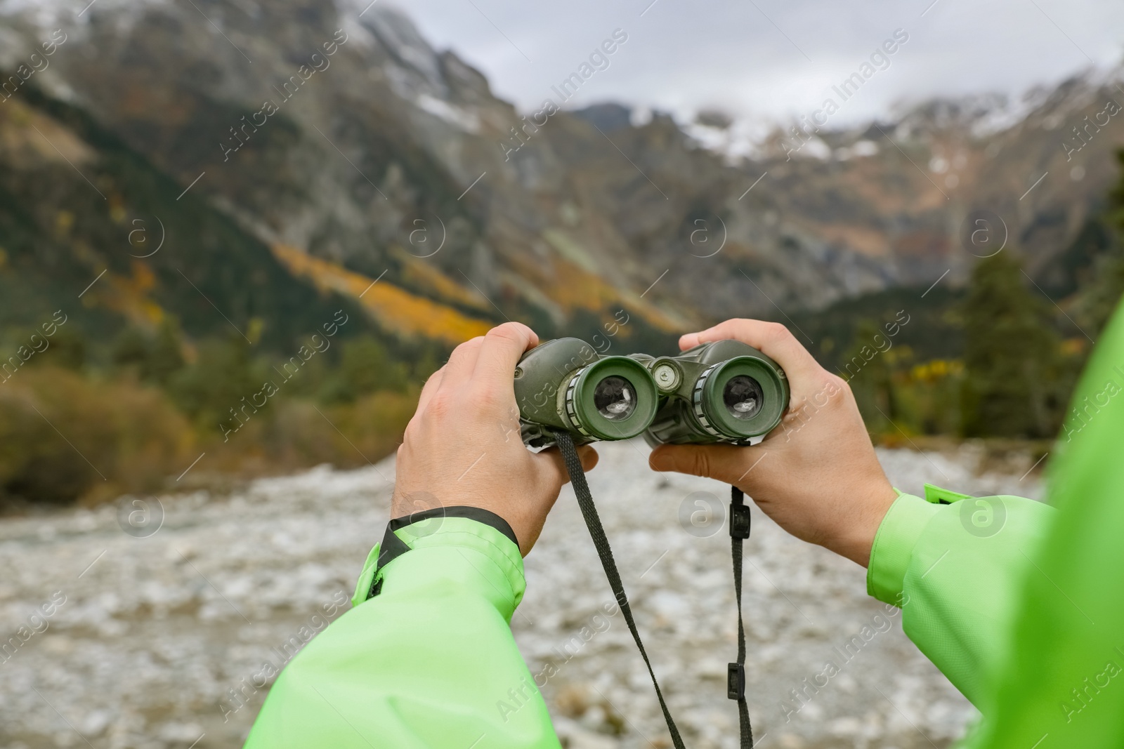 Photo of Woman holding binoculars near river in beautiful mountains, closeup. Space for text