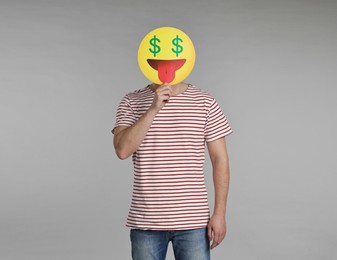 Photo of Man holding emoticon with dollar signs instead of eyes on grey background