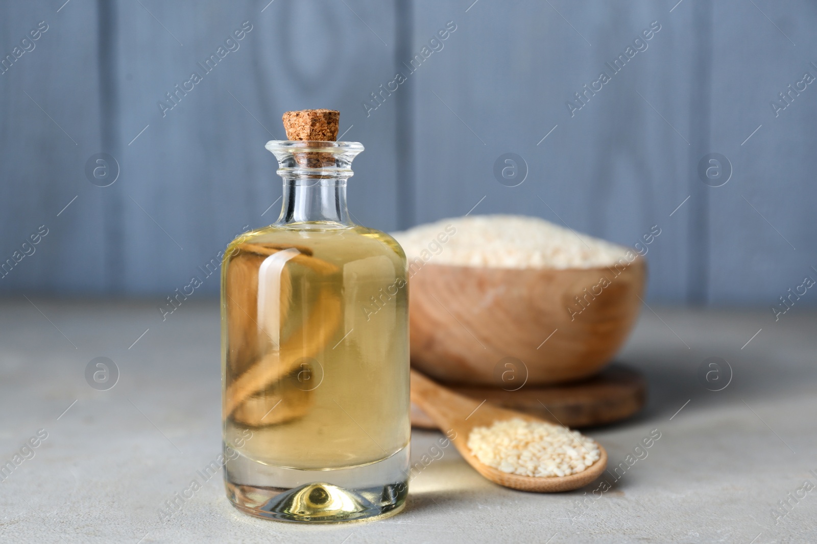Photo of Glass bottle of sesame oil and seeds on light grey table
