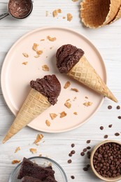 Chocolate ice cream scoops in wafer cones and candies on light wooden table, flat lay