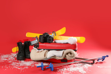 Suitcase with warm clothes, camera and skis on red background. Winter vacation