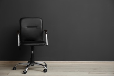 Comfortable office chair near black wall indoors. Space for text