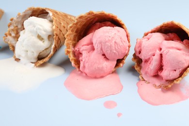 Melted ice cream in wafer cones on light blue background, closeup