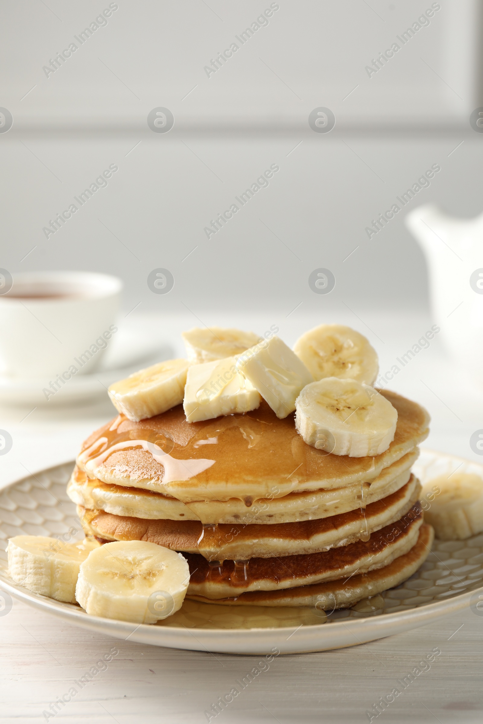 Photo of Delicious pancakes with bananas, honey and butter on white wooden table. Space for text