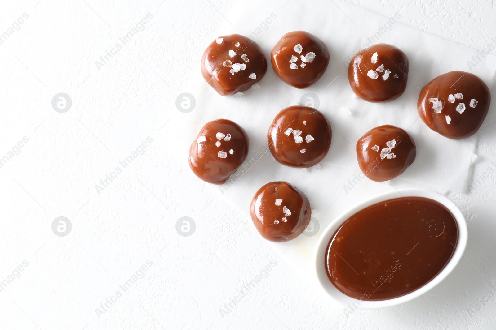Photo of Tasty candies, caramel sauce and salt on white table, top view. Space for text