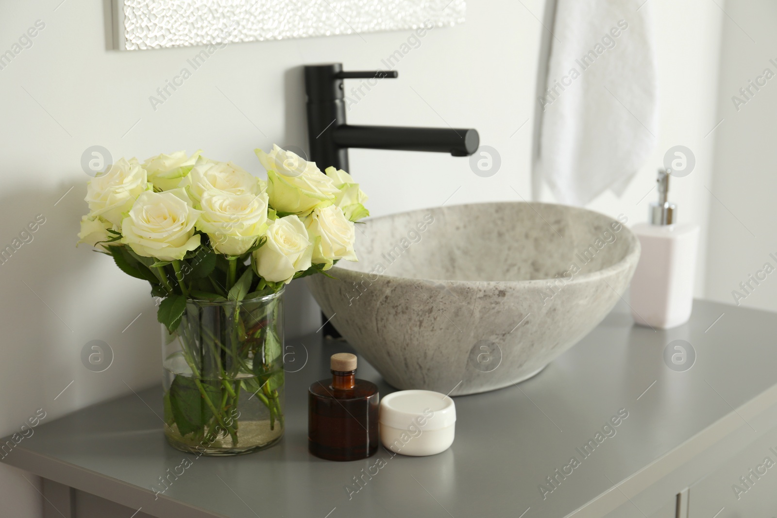 Photo of Vase with beautiful white roses and toiletries near sink in bathroom