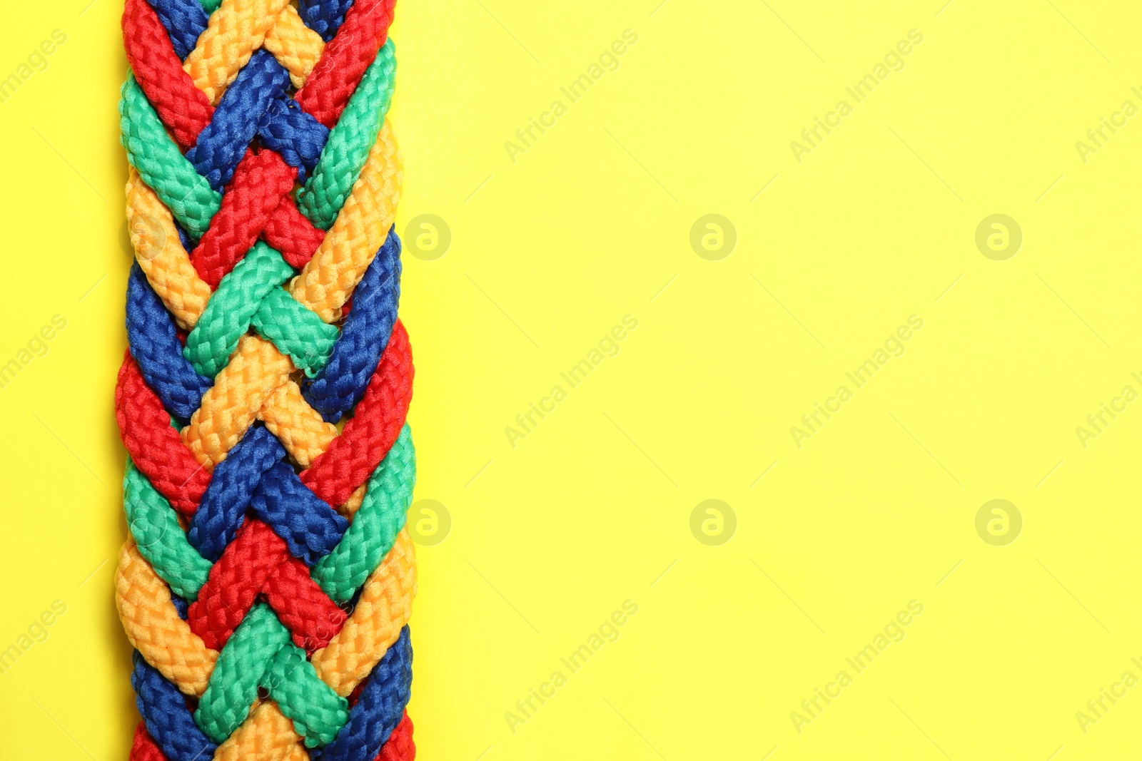 Photo of Top view of braided colorful ropes on yellow background, space for text. Unity concept