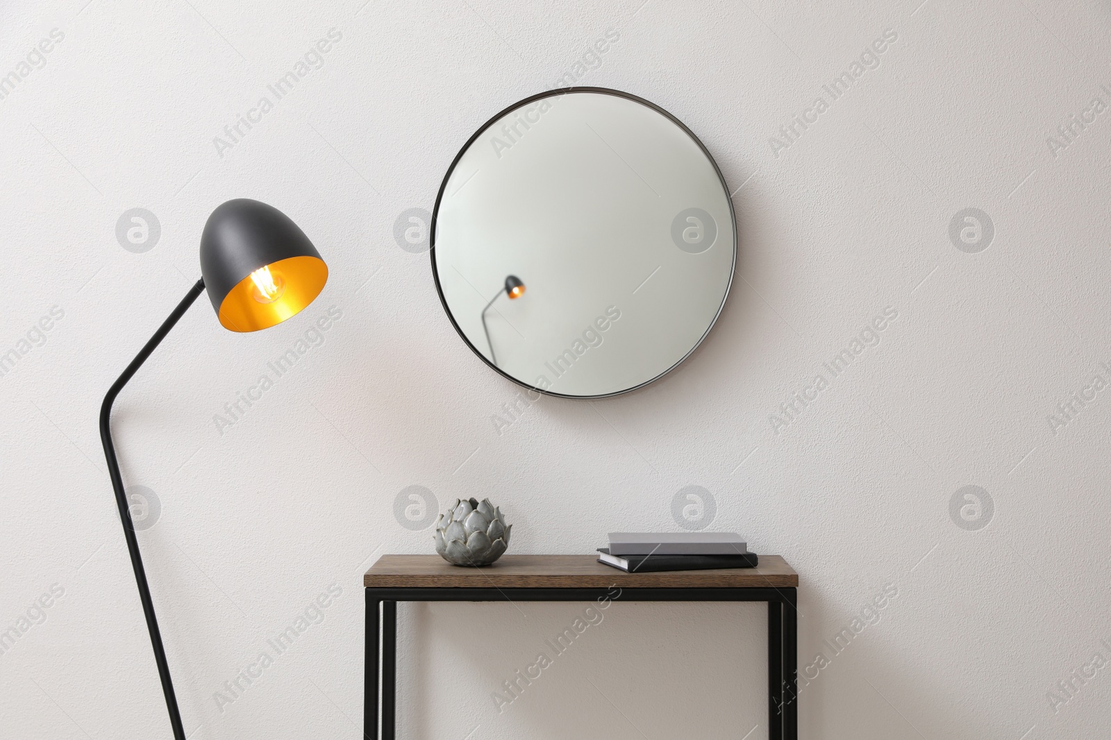 Photo of Console table and lamp near light wall with mirror indoors. Interior design