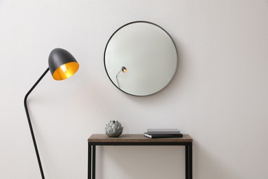 Photo of Console table and lamp near light wall with mirror indoors. Interior design