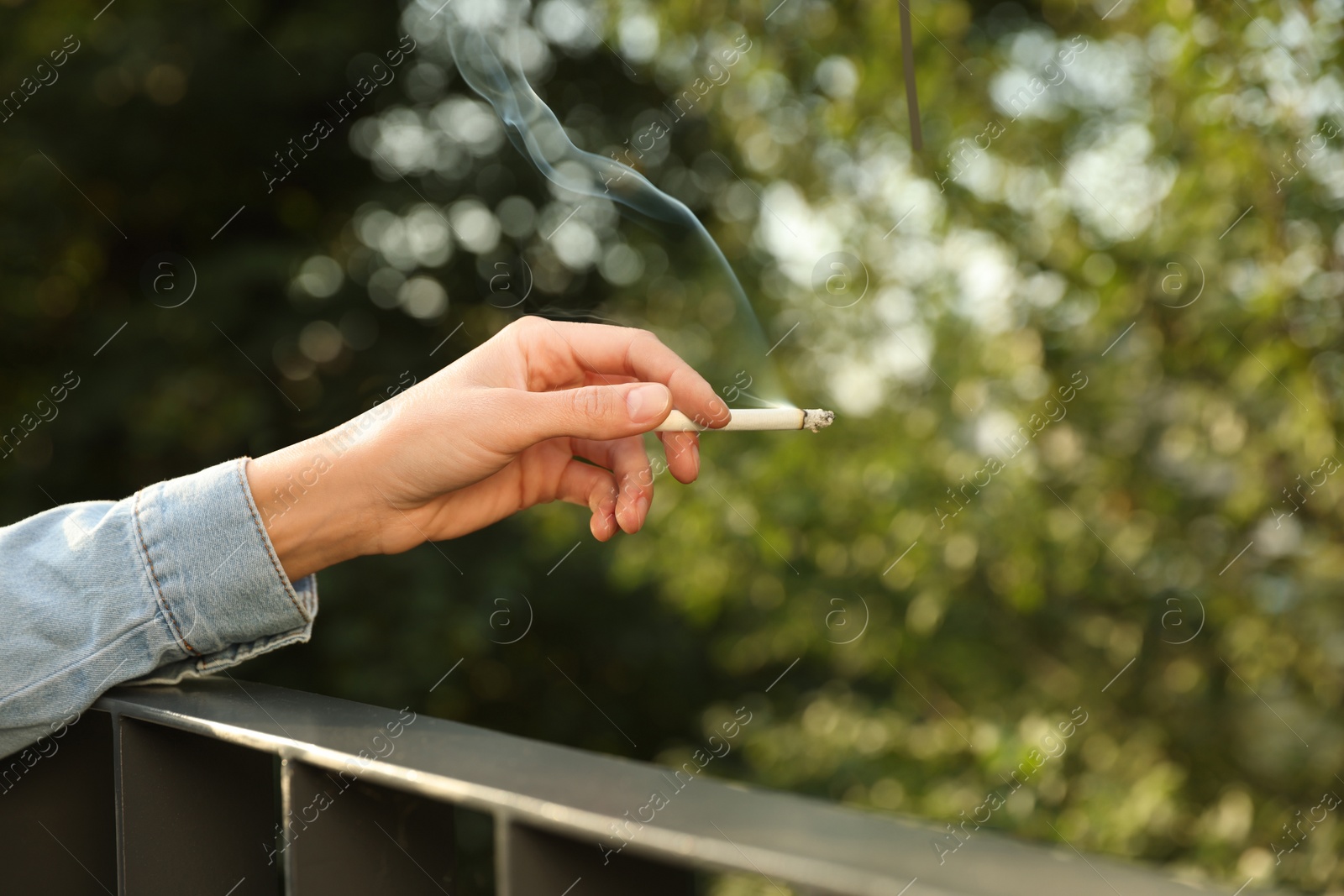 Photo of Woman smoking cigarette near railing outdoors, closeup of hand. Space for text