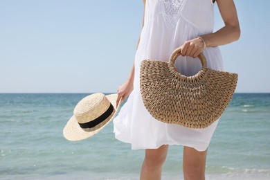 Photo of Woman with beach bag and straw hat near sea, closeup