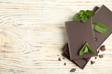 Photo of Tasty dark chocolate pieces with mint on white wooden table, flat lay. Space for text