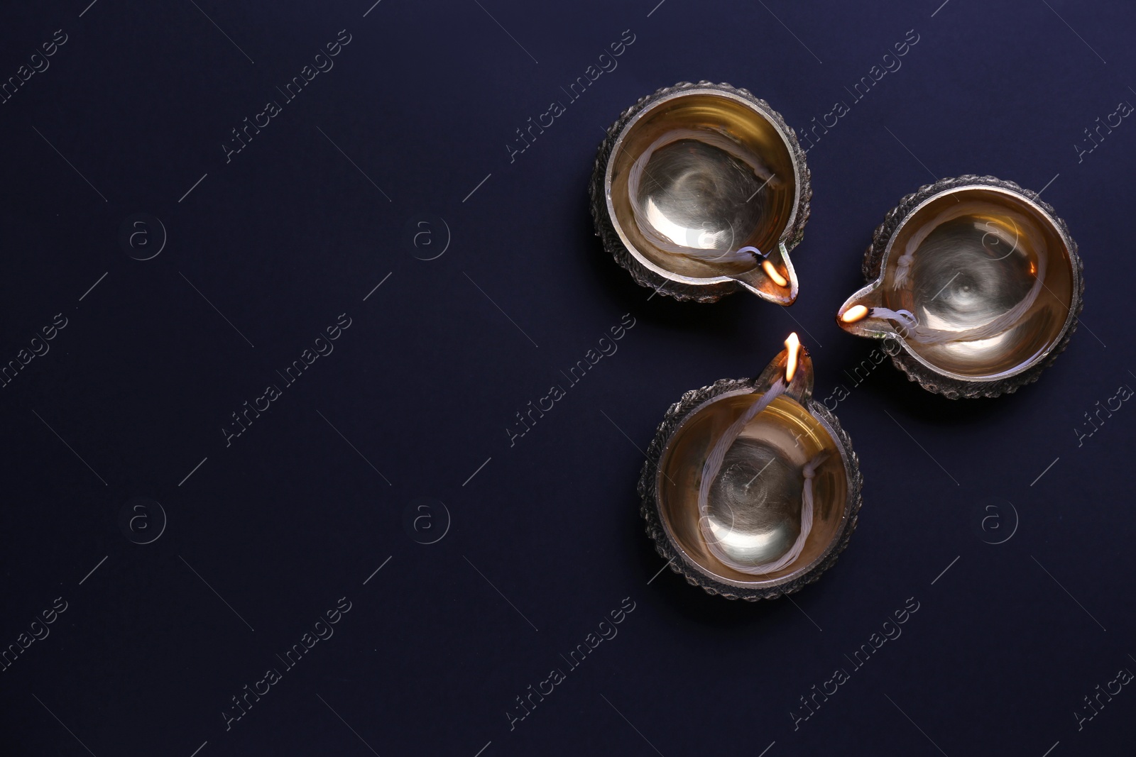 Photo of Lit diyas on dark background, flat lay with space for text. Diwali lamps