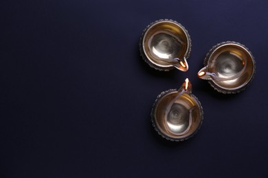 Photo of Lit diyas on dark background, flat lay with space for text. Diwali lamps