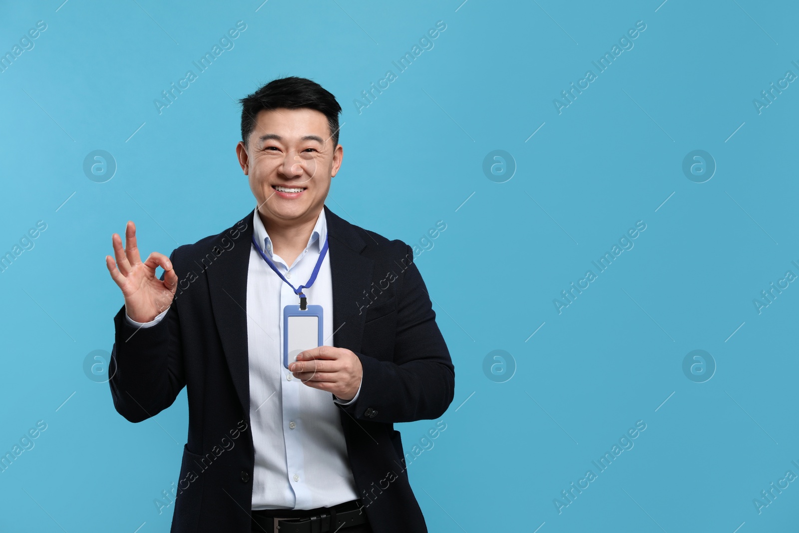 Photo of Happy asian man with vip pass badge showing ok gesture on light blue background. Space for text