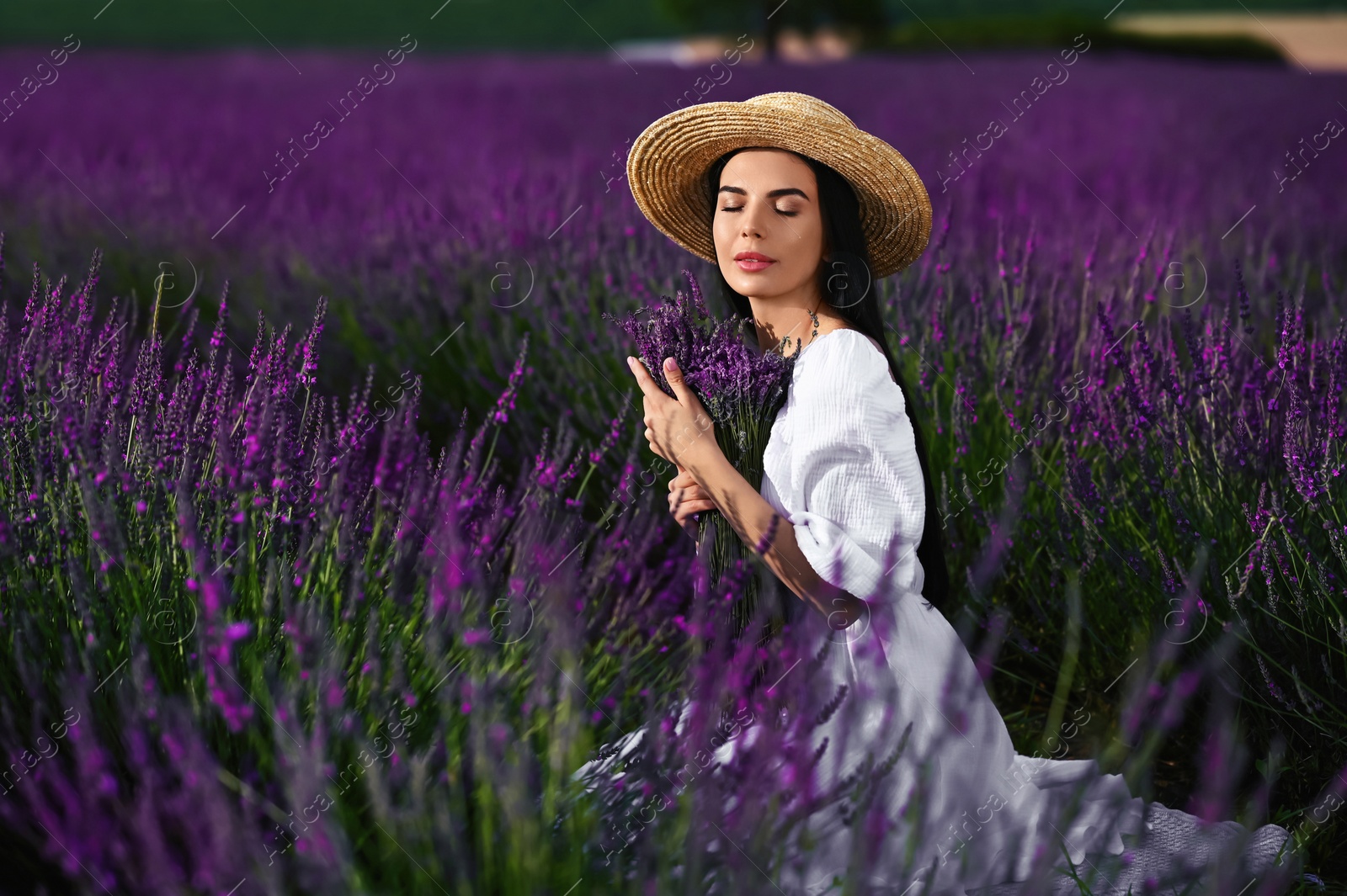 Photo of Beautiful young woman with bouquet sitting in lavender field