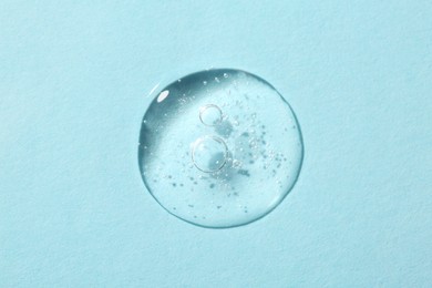 Drop of cosmetic serum on light blue background, top view