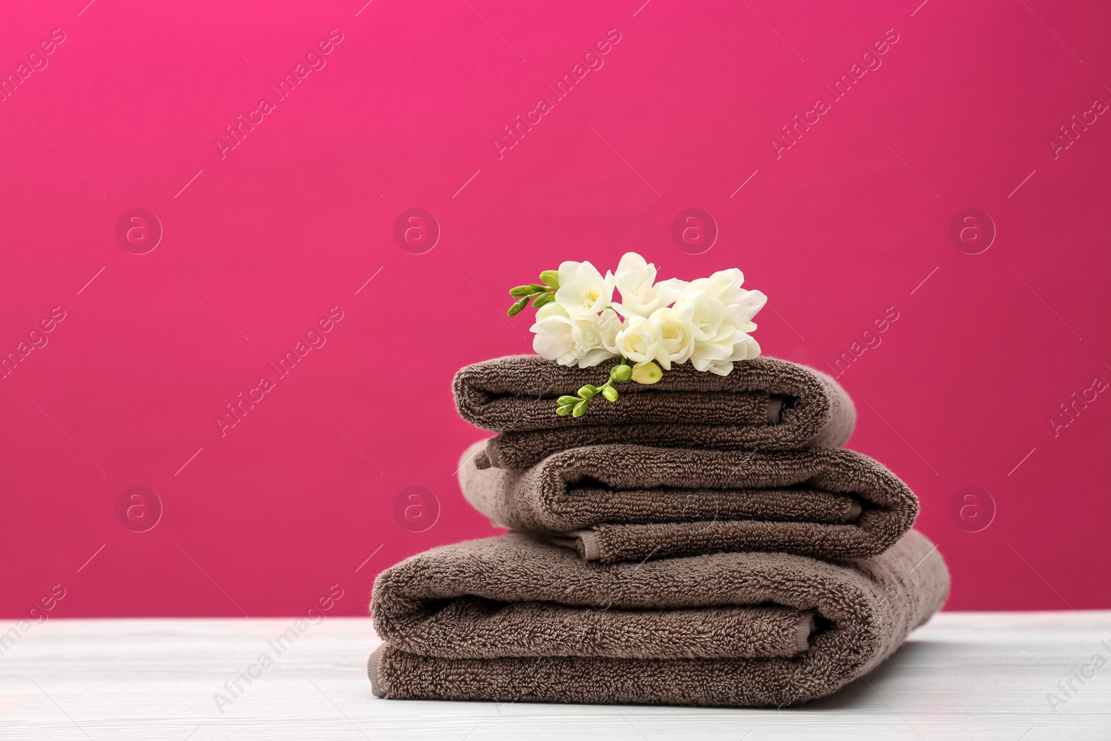 Photo of Stack of soft clean towels with beautiful flowers on table against color background. Space for text