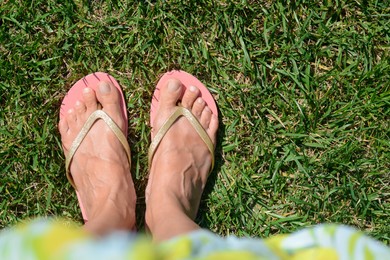 Woman wearing stylish flip flops on green grass outdoors, top view. Space for text