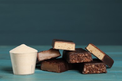Photo of Pieces of tasty bars and cup with protein powder on light blue wooden table. Space for text