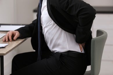 Photo of Businessman suffering from back pain at workplace, closeup