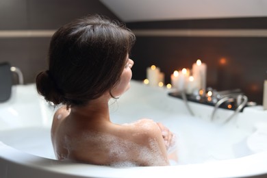 Photo of Young woman taking bubble bath, back view. Romantic atmosphere