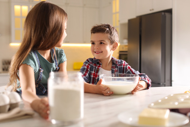 Photo of Cute little children cooking dough in kitchen at home