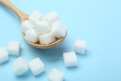 White sugar cubes and wooden spoon on light blue background, closeup. Space for text