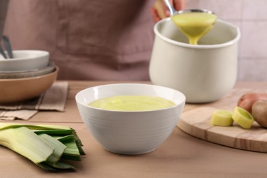 Photo of Woman with ladle pouring tasty leek soup at wooden table, focus on bowl
