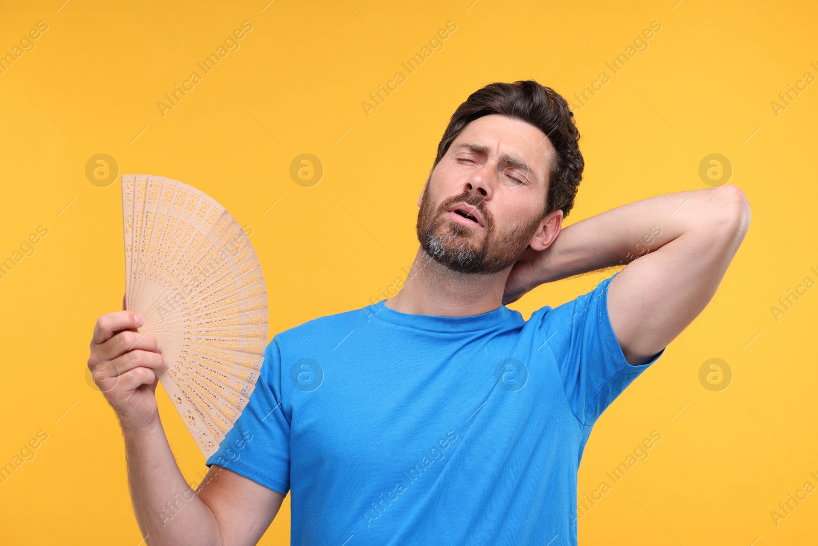 Photo of Unhappy man with hand fan suffering from heat on orange background