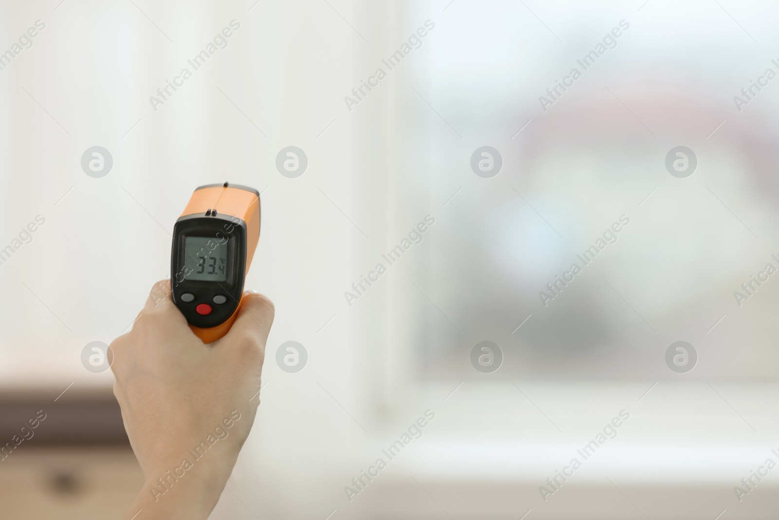 Photo of Closeup view of woman with infrared thermometer on blurred background, space for text. Checking temperature during Covid-19 pandemic