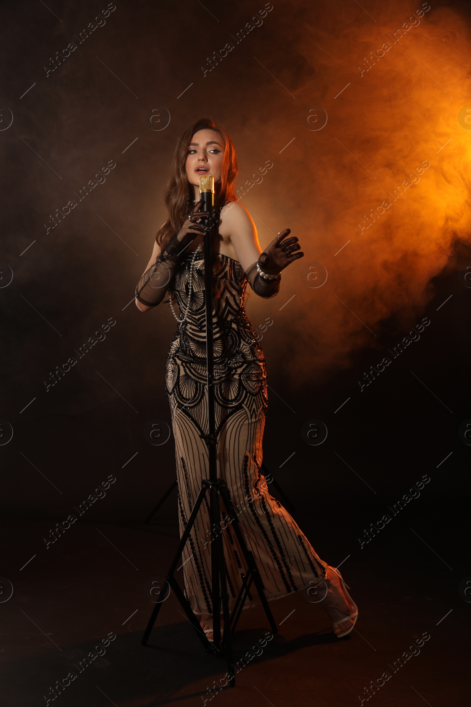 Photo of Beautiful young woman with microphone singing in color lights and smoke