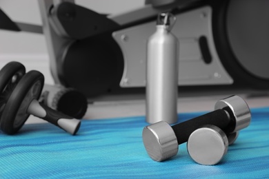 Dumbbells and sport equipment near elliptical machine in gym