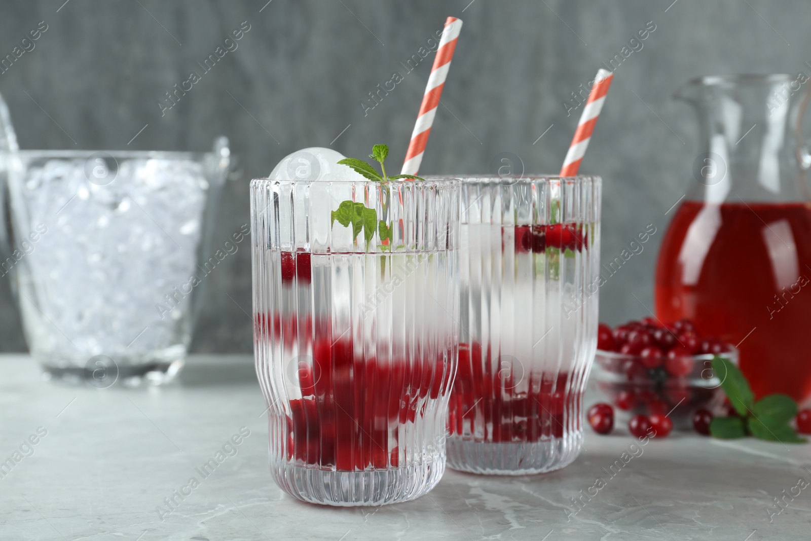Photo of Delicious cocktails with cranberries, mint and ice balls on grey table