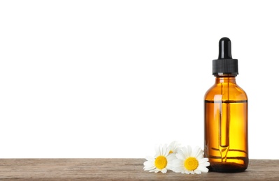 Bottle of chamomile essential oil and flowers on wooden table, white background