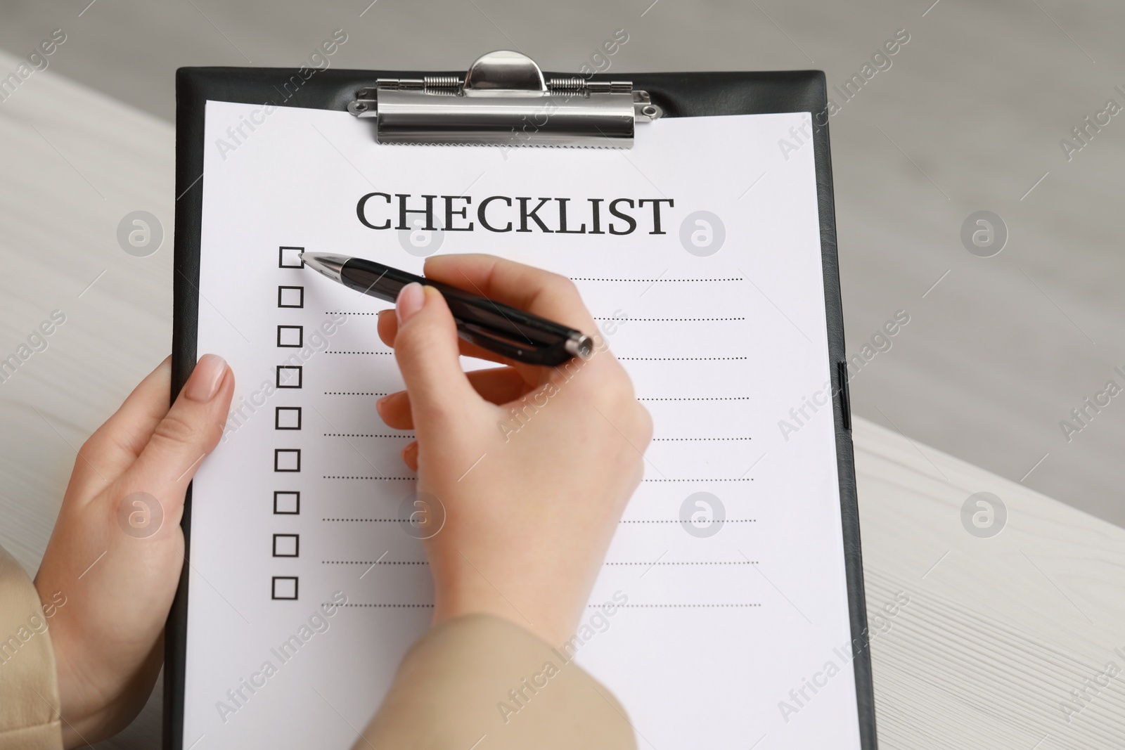 Photo of Woman filling Checklist at white wooden table, closeup