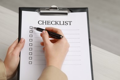 Woman filling Checklist at white wooden table, closeup