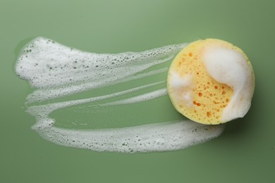 Yellow sponge with foam on green background, top view