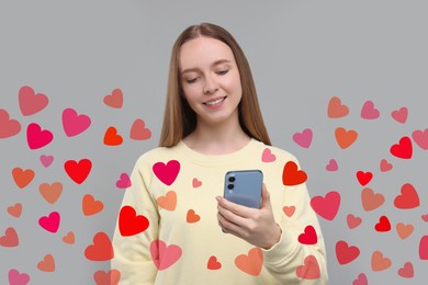 Image of Long distance love. Woman chatting with sweetheart via smartphone on grey background. Hearts around her