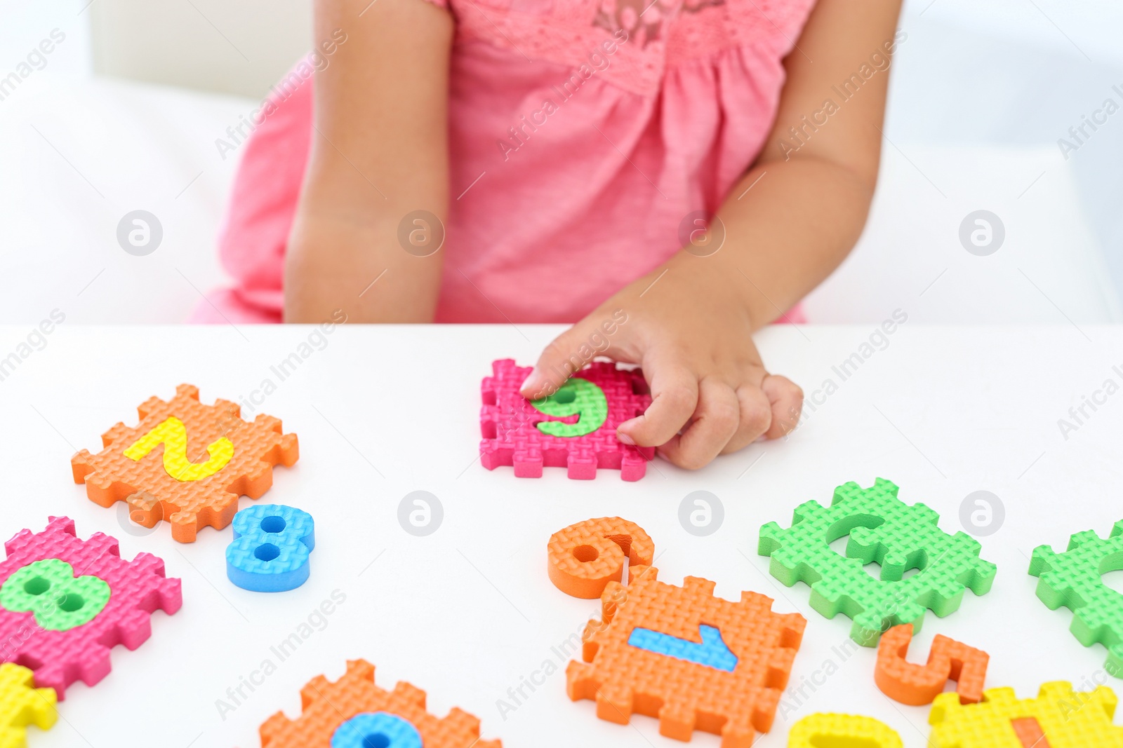 Photo of Little girl playing with colorful puzzles at white table, closeup. Educational toy