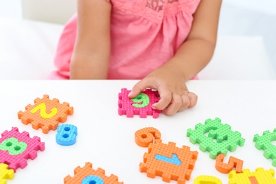 Photo of Little girl playing with colorful puzzles at white table, closeup. Educational toy